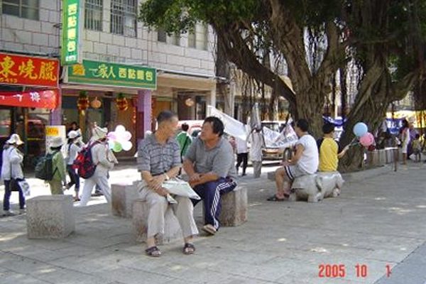 10月1日金门街道，悠闲的人们在榕树下看“金门声援500万人退出共产党”游行队伍，谈论著退党的消息。(大纪元)