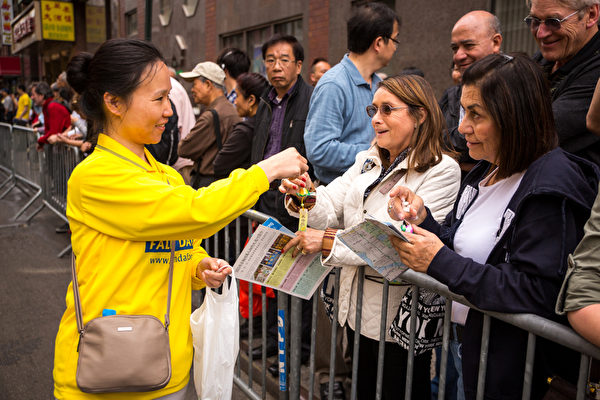2013年5月18日，紐約曼哈頓，來自世界各地的法輪功學員舉行慶祝法輪大法弘傳21週年大遊行。圖為法輪功學員將法輪功真相材料和小蓮花贈送給馬路旁圍觀的民眾。（攝影：陳虎／大紀元）