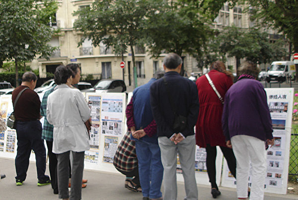 大陸遊客聚集在巴黎退黨服務中心的展板前，主動了解真相。（大紀元）