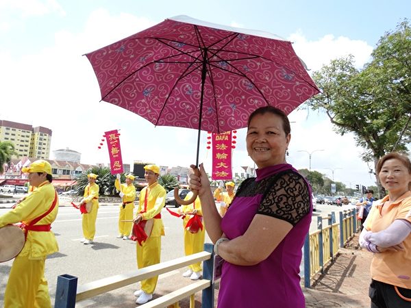 邓女士开心的撑着雨伞站在路旁观看游行。（徐长乐/大纪元）