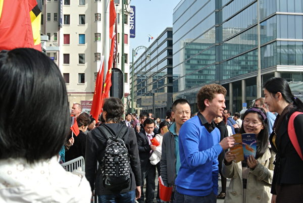 赶来酒店前的神韵主办方跟围住海报的华人讲真相。告诉他们神韵演出内容是弘扬真正的中国传统文化，备受全球海外人士推崇。（马丽／大纪元）