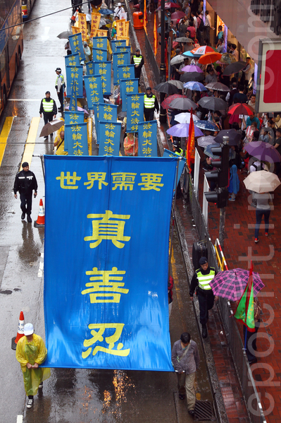六百多名香港及来自亚洲地区的法轮功学员5月10日冒雨游行，庆祝法轮大法洪传世界22周年，希望将法轮大法的美好传给世人，并呼吁民众三退“解体中共”，制止中共活摘人体器官等暴行。声势浩大的游行队伍途径港岛的闹市区，吸引许多市民和大陆游客撑着伞在路旁观看。（潘在殊/大纪元）