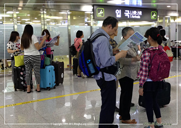 韓國濟州機場國際線到達廳裡中國遊客不斷。遊客們正在閲讀法輪功真相報紙（明慧網）。