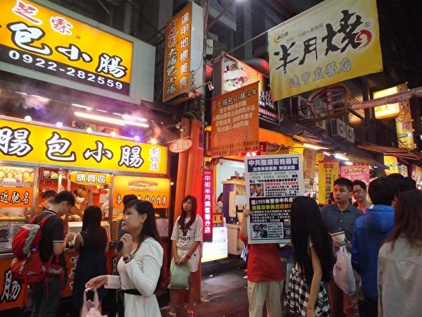 在台湾台中逢甲夜市知名摊贩前，排队的人龙不时望向法轮功真相展板。（黄玉燕／大纪元）