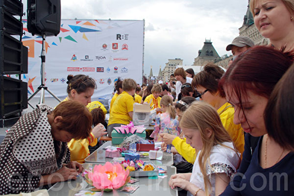 2012年5月27日，俄罗斯法轮功学员，参加了约10万人的大型运动庆祝活动。一旁设有15张桌子来折纸莲花。由于索要者众，许多人根本无法接近折莲花的桌子。