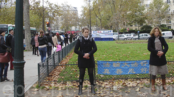 2013年11月11日，在巴黎退黨服務中心的真相橫幅和展板旁，法國的西人法輪功學員通過法輪功功法向中國遊客展示法輪大法的美好，用實際行動戳破中共的謊言。（大紀元）