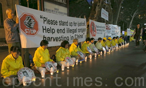 穿黃色衣服的法輪功學員手中捧著被迫害致死的法輪功學員的相片，靜靜地坐在悉尼市中心的喬治街，每個人前面的地上放著一盞點亮的燭燈。（摄影何蔚/大纪元）