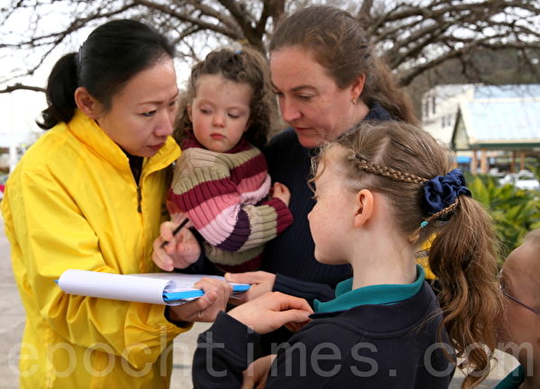 查理诺（Challinor）女士一手抱着最小的女儿，一手拿过笔在请愿书上签了名。然后，她把请愿书递给站在旁边的女儿们，让她们一一签名。（摄影：何蔚/大纪元）