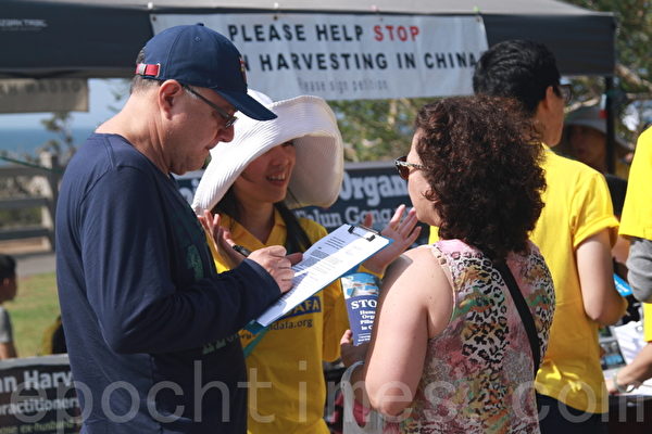 民眾在聖莫妮卡法輪功真相點前的反活摘徵簽表上簽字，並聽法輪功學員講真相。（張岳/大紀元）