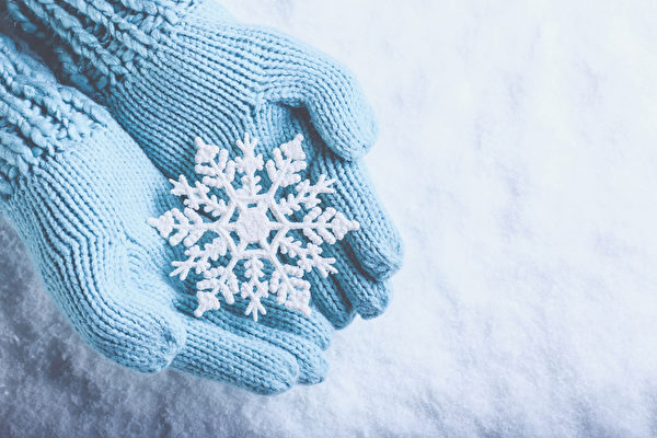 女手在光蓝绿色的针织手套与雪的背景闪闪发光精彩的雪花。冬季和圣诞节的概念（fotolia）
