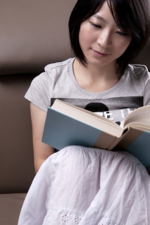 Portrait of a young woman sitting on sofa reading book(shutterstock)