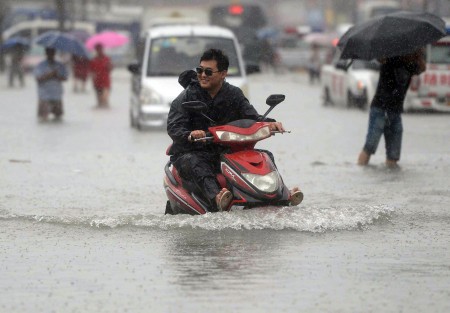 7月20日北京街头，一个男子开车摩托车涉水前行。（STR/AFP/Getty Images)