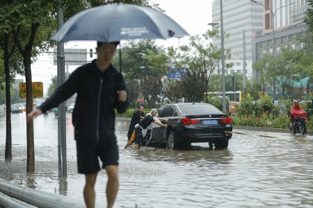 7月20日北京街头，人们奋力推沦陷在水中的车。(Lintao Zhang/Getty Images)