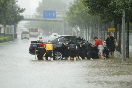 7月20日北京街头，人们奋力推沦陷在水中的车。(Lintao Zhang/Getty Images)