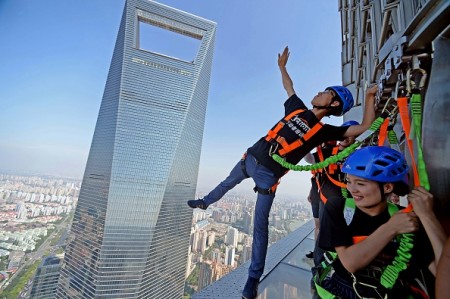 This photo taken on July 25, 2016 shows a visitor (L) balancing on an open-air glass walkway with other visitors outside the 88th floor of Jinmao Tower in the Lujiazui area of Shanghai. The 60-metre long and 1.2-meter wide walkway is officially open to the public from July 28. / AFP / STR / China OUT (Photo credit should read STR/AFP/Getty Images)