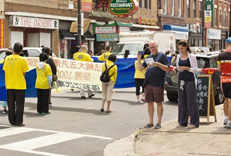 2016年7月30日，来自中部十个州的法轮功学员汇集在芝加哥中国城举行盛大的游行。图为观众边录像边阅读传单。（David Yang/大纪元）