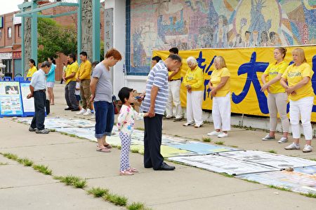 2016年7月30日，来自中部十个州的法轮功学员汇集在芝加哥中国城举行盛大的游行。图为华人民众阅读法轮功炼功点的真相展板。（陈杰杰/大纪元）