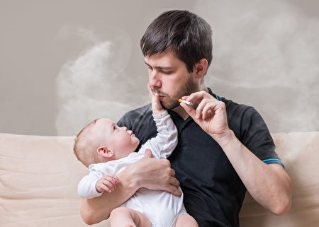 Bad father is smoking and holding little baby in hands.