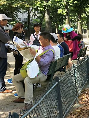 大陆游客在巴黎埃菲尔铁塔下休息时，认真阅读法轮功学员发送给他们的《真相报》。（明慧网）