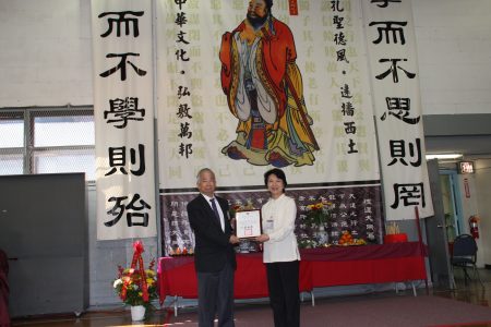 徐儷文（右）代表中華民國僑務委員會委員長吳新興，向剛卸任的老校長黃炯常（左）頒發「功在僑校」的賀匾。