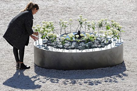 悼念仪式上，一名遇害者家属在花坛里插上一枝白玫瑰。 ( VALERY HACHE/AFP/Getty Images)