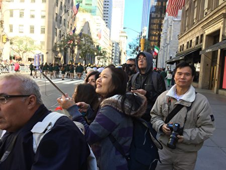 华人观看哥伦布日游行，兴奋地用自拍竿拍照。