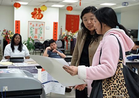 華人選民（右）在樂宜居投票站，正要將選票插入計票機，選舉義工陳本恩（左）進行協助翻譯。（溫文清/大紀元） 