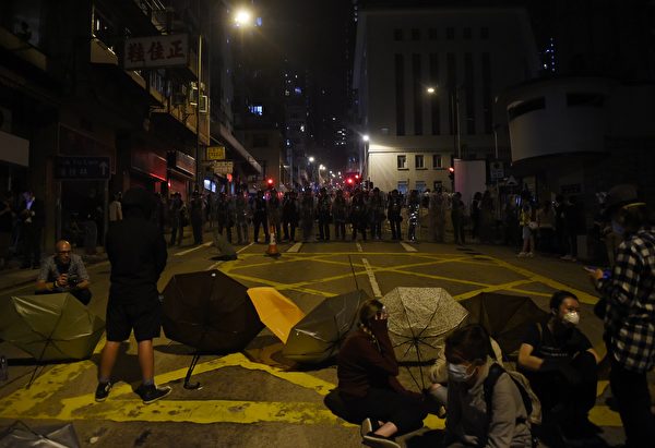 Police block off a street as protesters sit with umbrellas amid ongoing protests in Hong Kong on November 6, 2016. Hong Kong police used pepper spray November 6 to drive back hundreds of protesters angry at China's decision to intervene in a row over whether two pro-independence lawmakers should be barred from the city's legislature. In chaotic scenes reminiscent of mass pro-democracy protests in 2014, demonstrators charged metal fences set up by police outside China's liaison office in the semi-autonomous city. / AFP / Anthony WALLACE (Photo credit should read ANTHONY WALLACE/AFP/Getty Images)