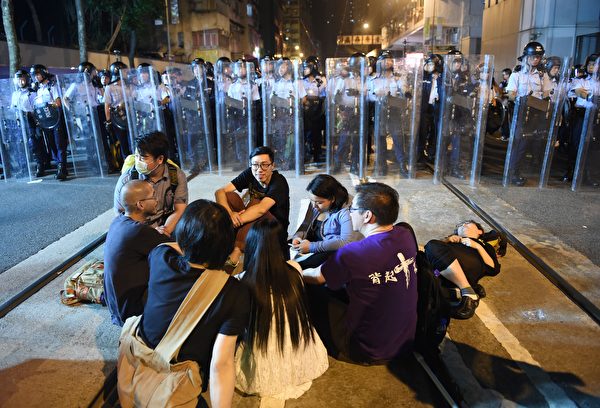 Protesters sit on a main street which has been blocked off as police in riot gear hold shields as they stand guard amid ongoing protests in Hong Kong on November 6, 2016. Hong Kong police used pepper spray November 6 to drive back hundreds of protesters angry at China's decision to intervene in a row over whether two pro-independence lawmakers should be barred from the city's legislature. In chaotic scenes reminiscent of mass pro-democracy protests in 2014, demonstrators charged metal fences set up by police outside China's liaison office in the semi-autonomous city. / AFP / Anthony WALLACE (Photo credit should read ANTHONY WALLACE/AFP/Getty Images)
