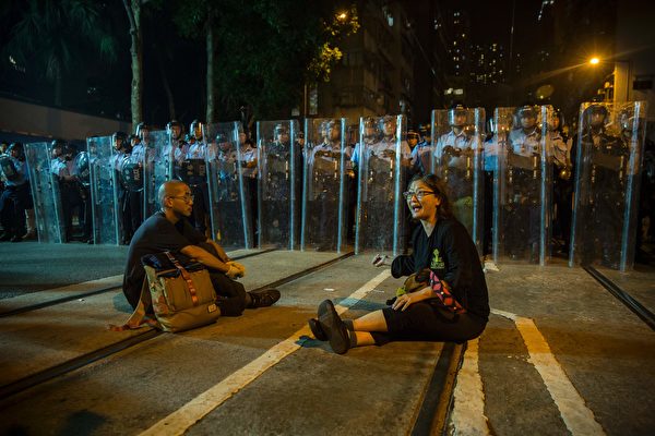 Protesters sit in a road as police in riot gear stand guard amid ongoing demonstrations in Hong Kong on November 6, 2016. Hong Kong police used pepper spray November 6 to drive back hundreds of protesters angry at China's decision to intervene in a row over whether two pro-independence lawmakers should be barred from the city's legislature. In chaotic scenes reminiscent of mass pro-democracy protests in 2014, demonstrators charged metal fences set up by police outside China's liaison office in the semi-autonomous city. / AFP / ISAAC LAWRENCE (Photo credit should read ISAAC LAWRENCE/AFP/Getty Images)