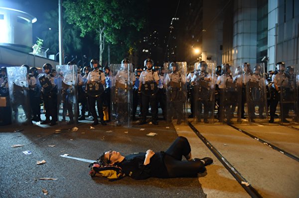 A protesters lies on a blocked street as police in riot gear stand guard amid ongoing protests in Hong Kong on November 6, 2016. Hong Kong police used pepper spray November 6 to drive back hundreds of protesters angry at China's decision to intervene in a row over whether two pro-independence lawmakers should be barred from the city's legislature. In chaotic scenes reminiscent of mass pro-democracy protests in 2014, demonstrators charged metal fences set up by police outside China's liaison office in the semi-autonomous city. / AFP / Anthony WALLACE (Photo credit should read ANTHONY WALLACE/AFP/Getty Images)