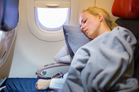 Tired blonde casual caucasian lady napping on uncomfortable seat while traveling by airplane. Commercial transportation by plane