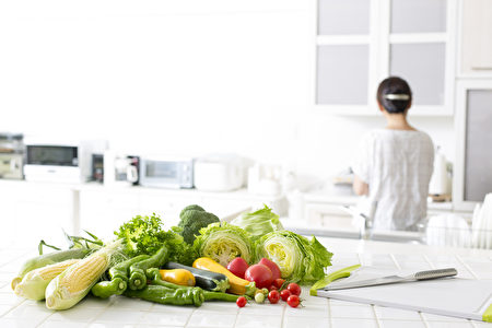 女人在廚房做菜。一堆蔬菜，健康概念。