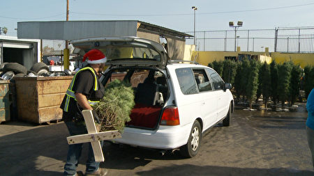 回收站工人頭戴聖誕老人的帽子，把樹放到人們的車上。（楊陽/大紀元）