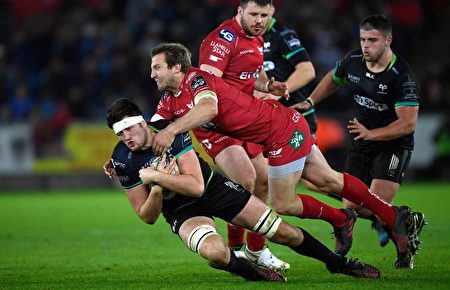 SWANSEA, WALES - DECEMBER 27: Scarlets centre Hadleigh Parkes tackles Rory Thornton of the Ospreys during the Guinness Pro 12 match between 頭戴繃帶者：我都受傷了，你能不能悠著點？ 紅衣人：不行啊，老兄，我也是身不由己啊！ 後面站立的紅衣人：（無語）。 黑衣人：當心，別閃著腰！ (Photo by Stu Forster/Getty Images)