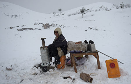 Afghan tea vendor Attaullah, 12, warms his hands as he waits for customers on a hillside during snowfall near Qargha Lake on the outskirts of Kabul on February 4, 2017. / AFP / WAKIL KOHSAR        (Photo credit should read WAKIL KOHSAR/AFP/Getty Images)